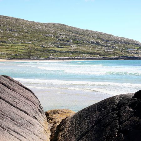 Coastal landscape in Ireland featuring a sandy beach bordered by smooth rocks, with a grassy hill overlooking the scene