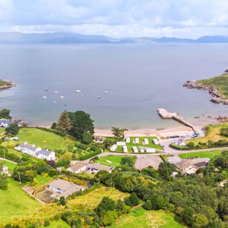 A bird's-eye view of a beautiful village in Ireland, situated by the sea, with boats moored in the bay and a backdrop of rolling hills and mountains
